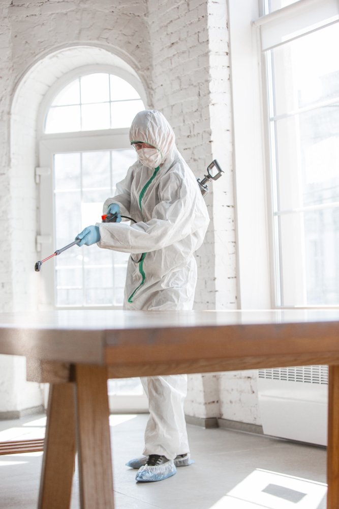 exterminator spraying an all white home with a brown wooden table in it